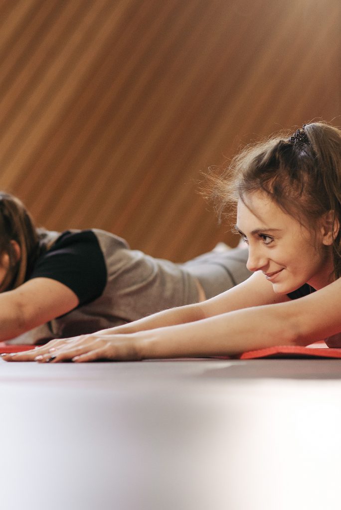 Two women happily stretching on mats in a bright, cozy studio setting.