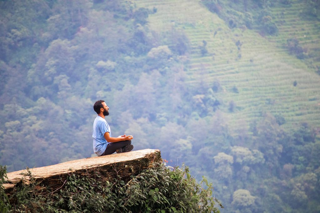 Man meditating on a cliff with lush green mountains in Ghandruk, Nepal.